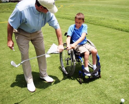 chlld in wheelchair golfing with instruction