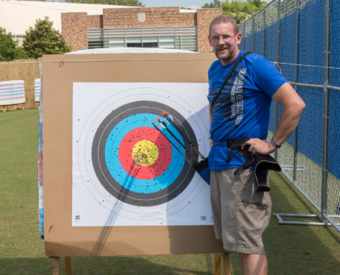 athlete standing next to target posing next to his arrows