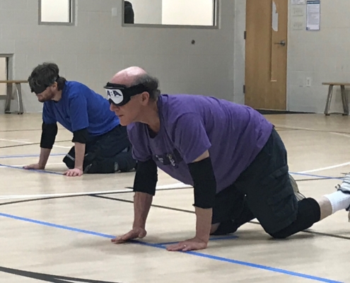 two goalball athletes on the floor preparing to defend