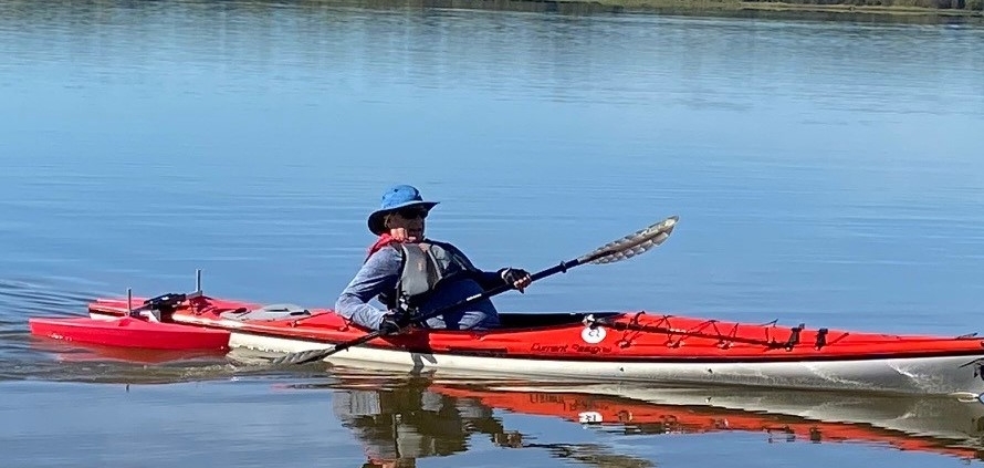 Man paddling in kayak with outriggers on back for stability